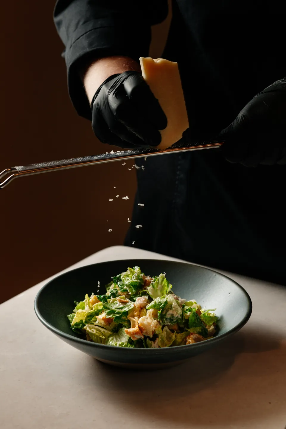 A chef finishing a fresh salad with grated cheese