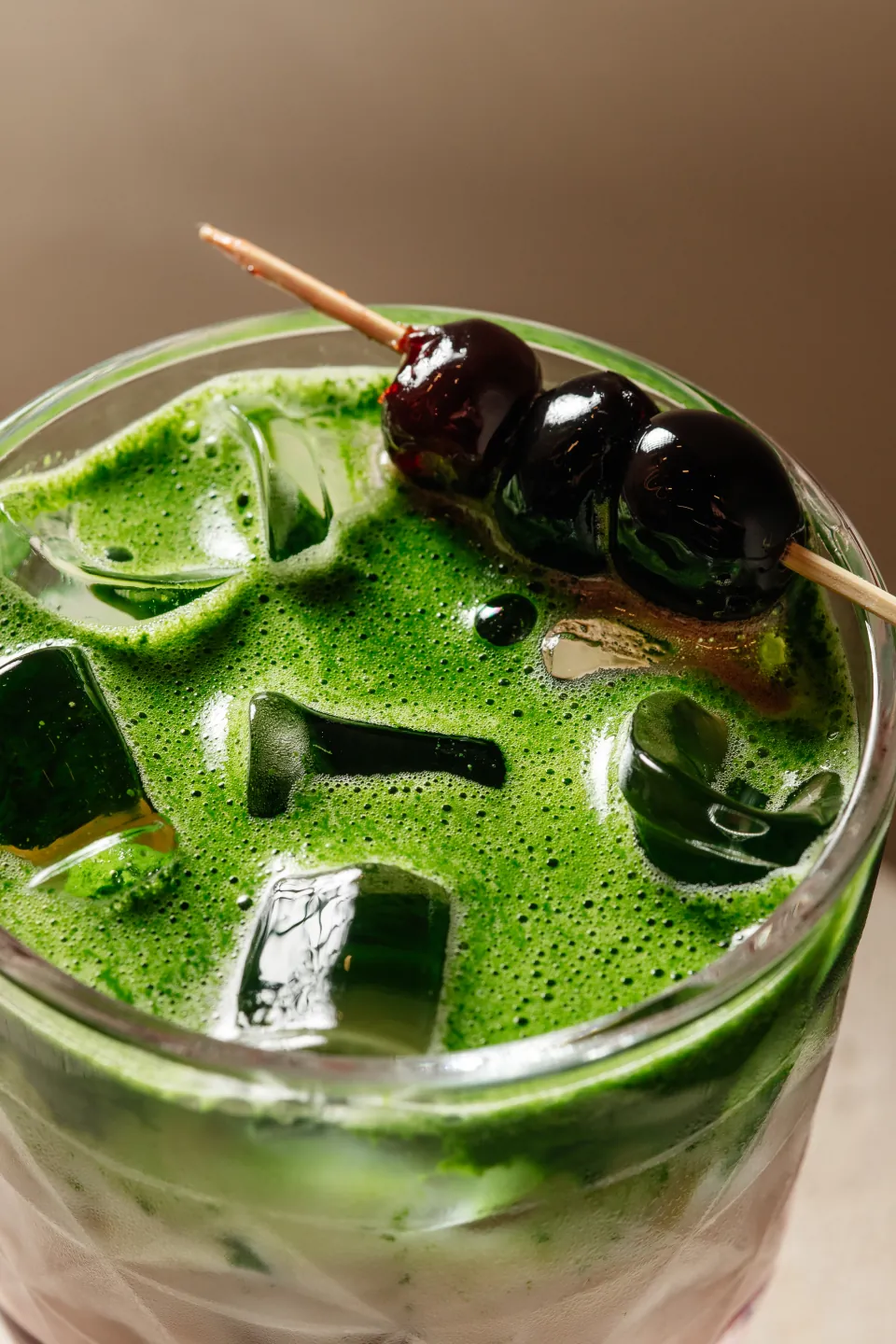 A close view of an iced green drink with cherries